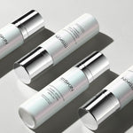 Four bottles of 111SKIN Dark Spot Correcting Serum arranged diagonally on a light grey background. The bottles have a sleek, pearlescent white design with silver caps and accents, casting soft shadows.