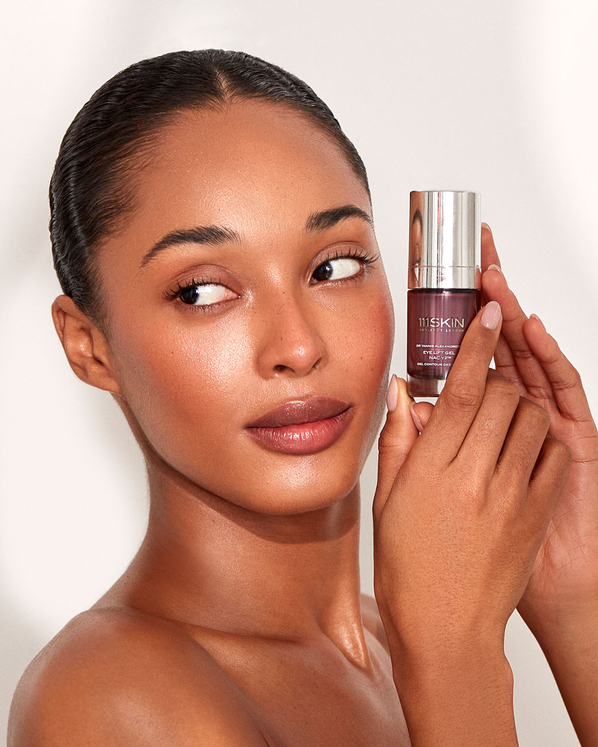 Model looking to the right while holding a bottle of 111skin Eye Gel