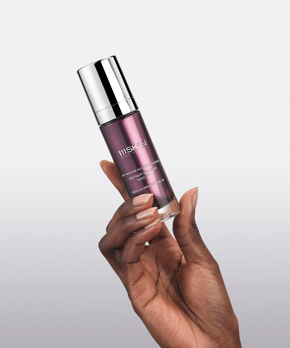 Hand holding a purple glass bottle of 111SKIN Repair Serum